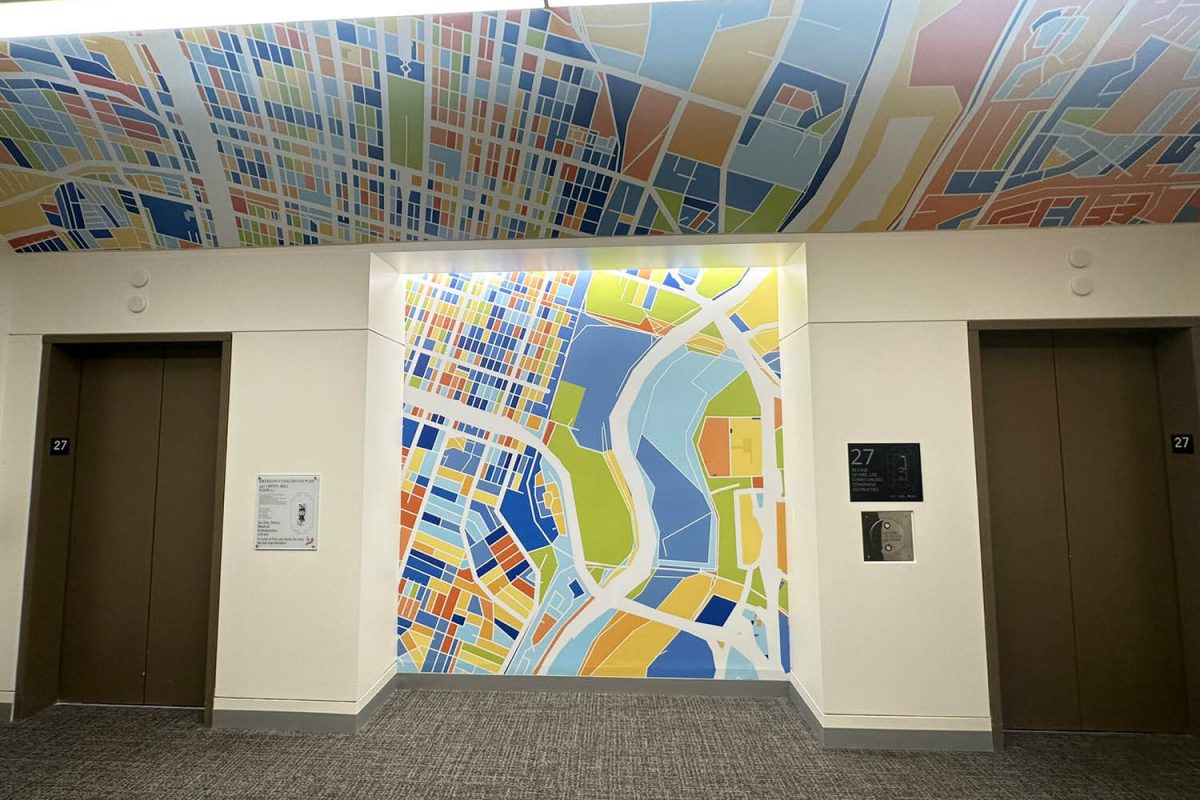 Colorful abstract map mural applied to the wall and ceiling of an elevator lobby, creating a vibrant visual feature between two elevator doors.