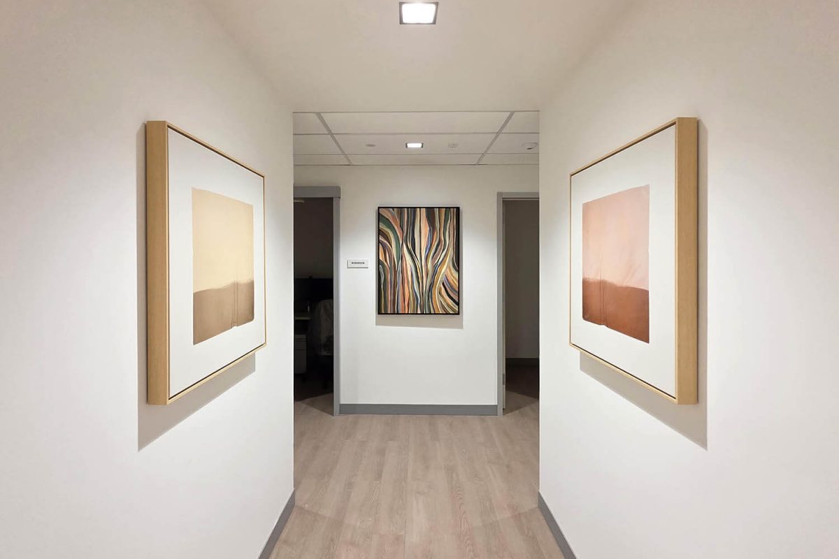 Hallway with minimalist framed artwork featuring soft color fields on the sides and an abstract multicolor piece at the end of the corridor.