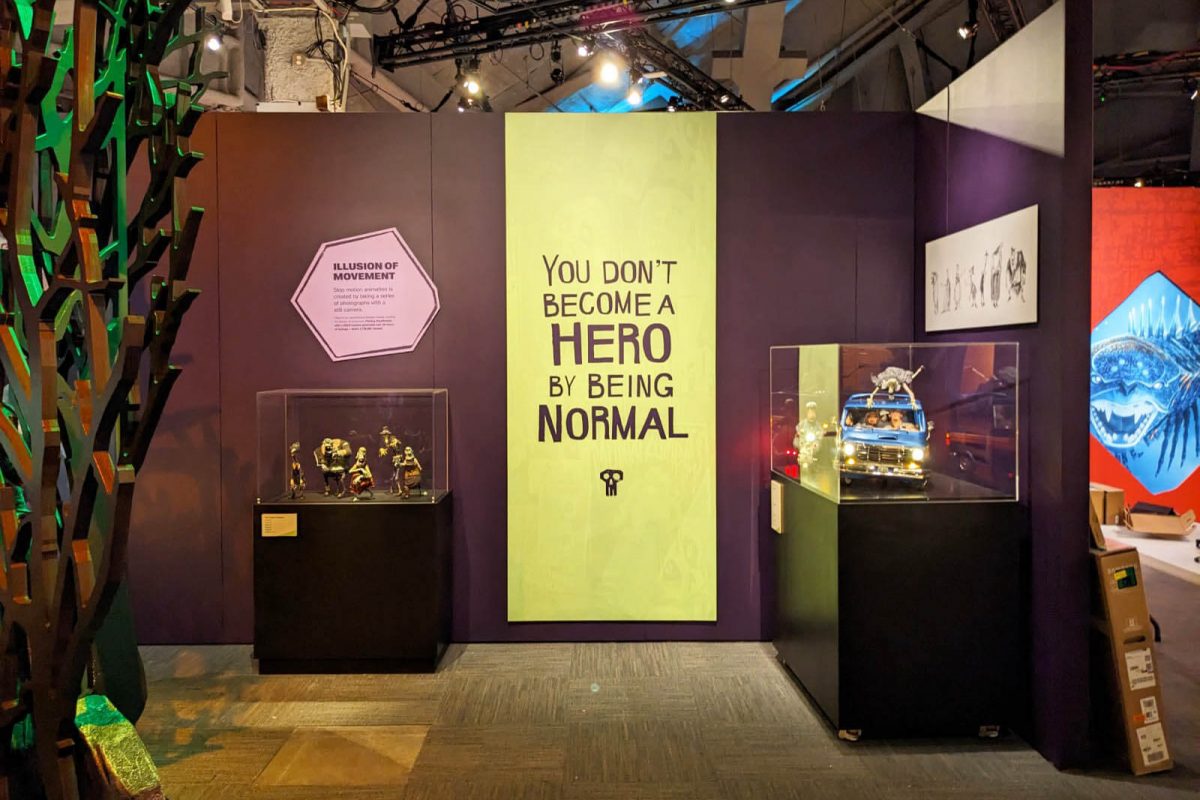 Exhibit wall from MoPOP’s Hidden Worlds: The Films of LAIKA featuring a bold typographic graphic reading “You don’t become a hero by being normal,” flanked by character models in display cases, produced and installed by SuperGraphics.