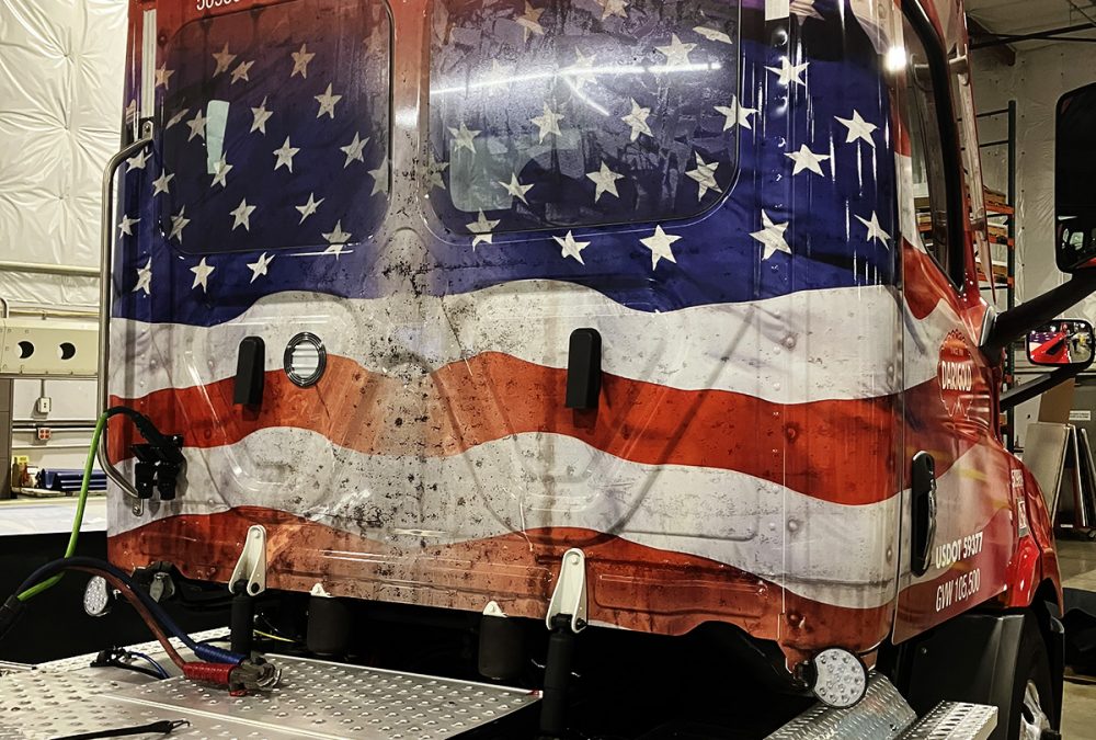 A red semi-truck wrapped with an American flag graphic and Darigold branding, emphasizing patriotic themes.