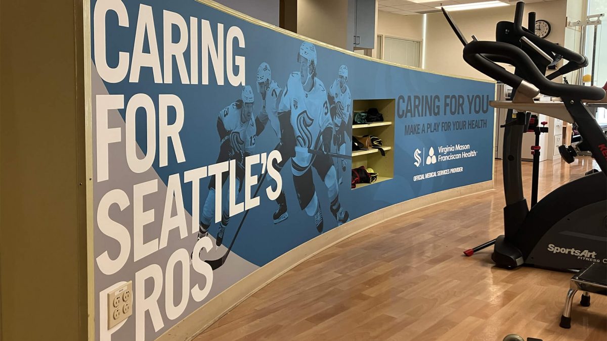 Seattle Kraken Wall Mural in athletic training facility, produced and installed by SuperGraphics. Message says "Caring for Seattle's Pros."