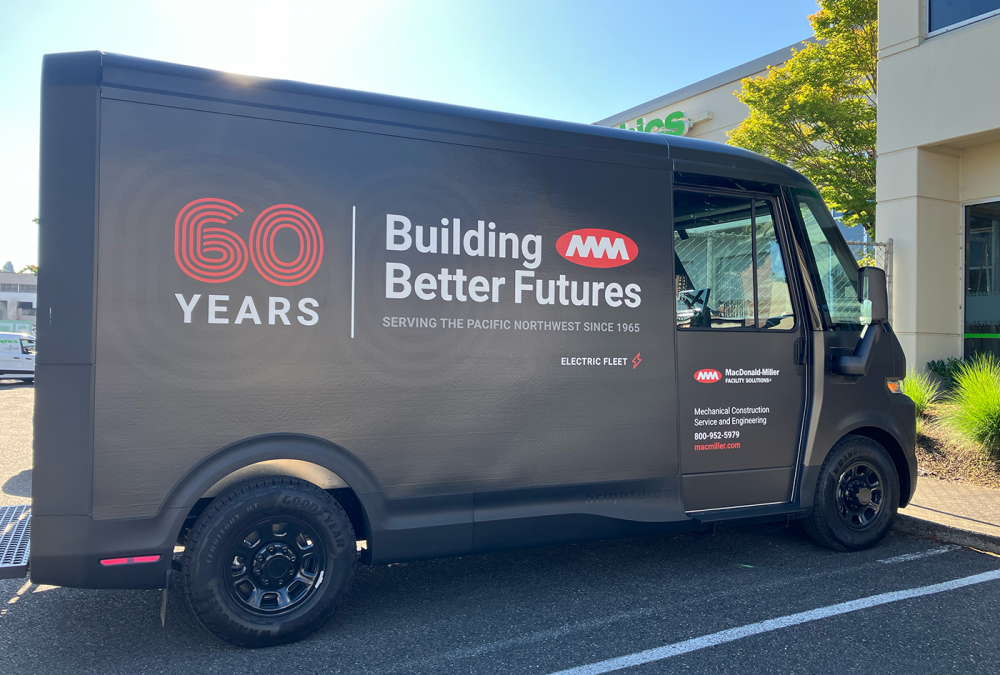MacDonald-Miller electric fleet van wrap on a matte black finish celebrating '60 YEARS' with corporate branding and 'Building Better Futures' message.