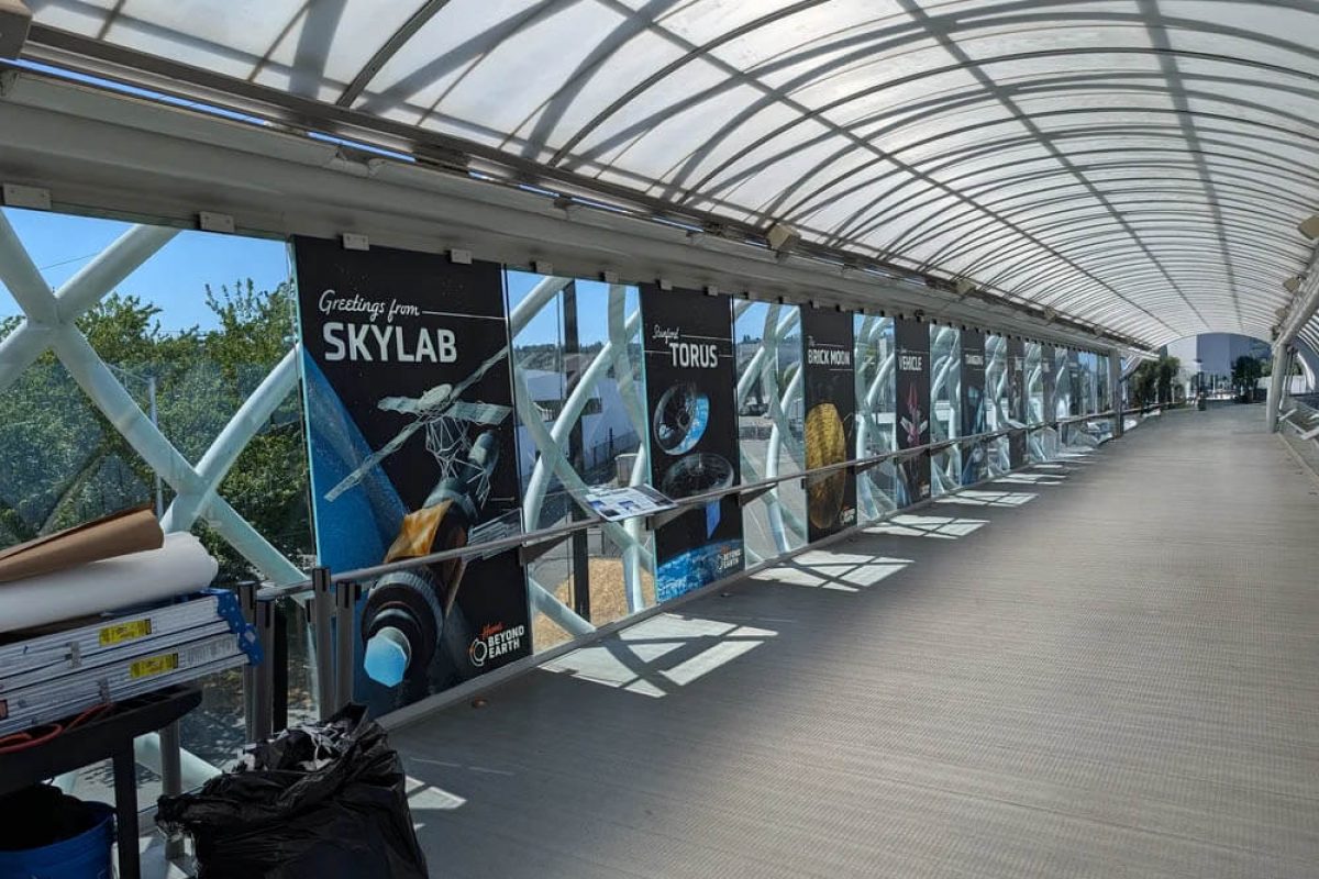 Long, glass-enclosed museum walkway featuring large-format space exploration graphics and interpretive panels, produced and installed by SuperGraphics.