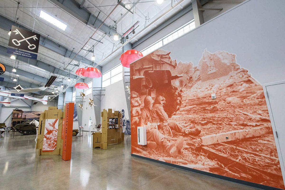 Aviation gallery at The Museum of Flight featuring large-scale sepia-toned wall graphics depicting WWII-era soldiers, surrounded by aircraft and interpretive displays, produced and installed by SuperGraphics.