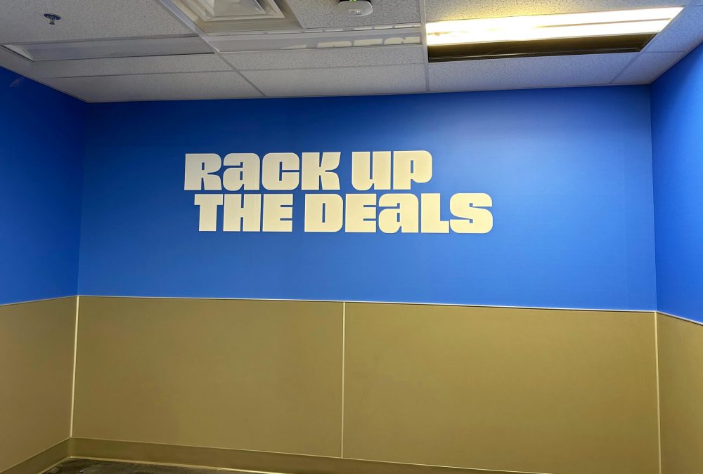 Nordstrom Rack wall mural, produced and installed by SuperGraphics. Graphic says 'Rack up the deals' in fitting room area.