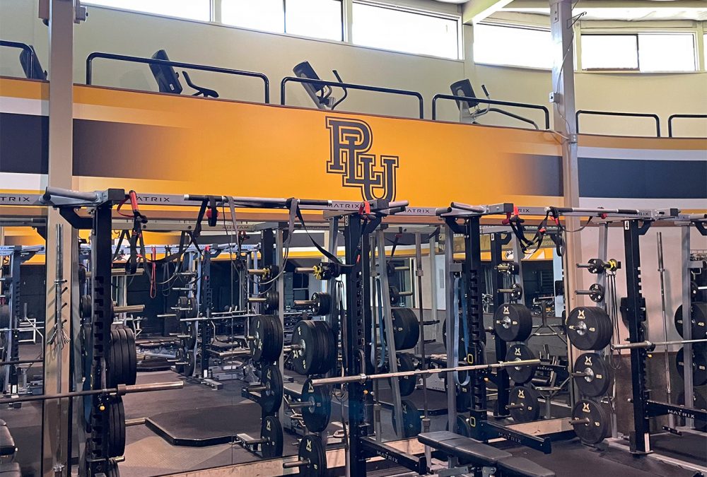 Pacific Lutheran University's Names Fitness Center, showcasing branding with soffit wall graphics in the weight room. School graphics enhance the space, reflecting the university's identity.