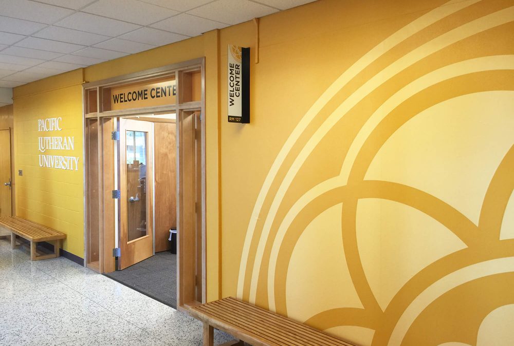 Pacific Lutheran University Welcome Center branding, produced and installed by SuperGraphics. Showcases large yellow wall murals with branded iconography.