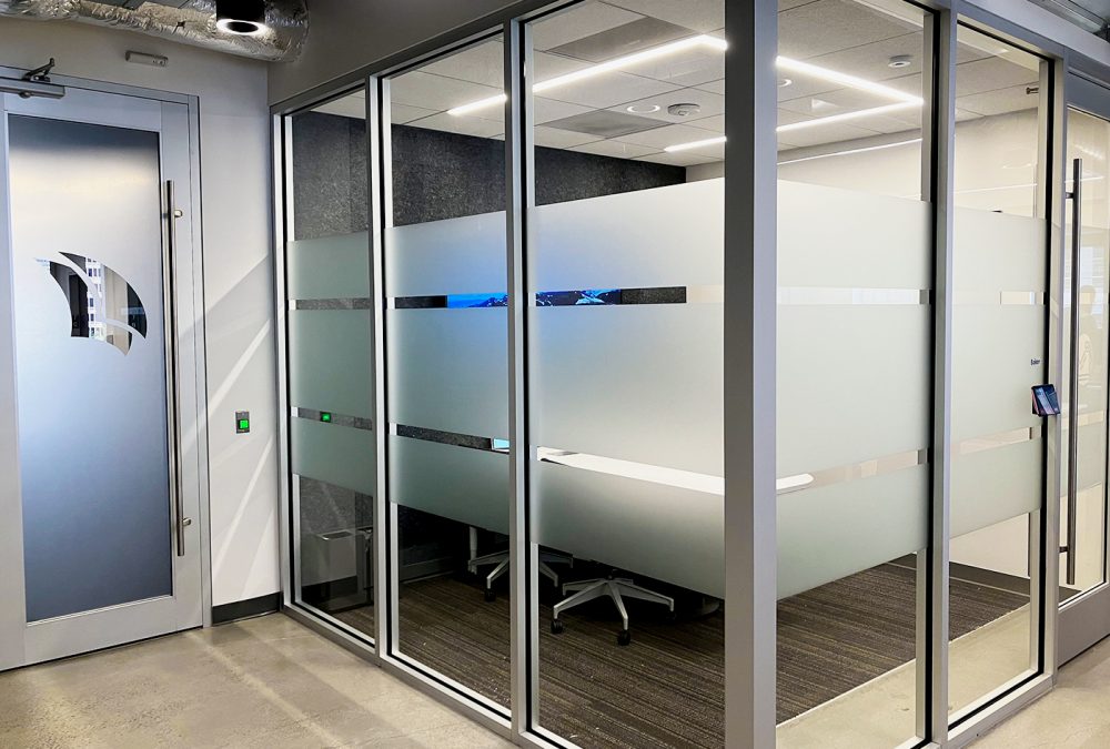Photo of privacy film window graphics in Pitchbook office, produced and installed by SuperGraphics. Showcases glass windows to corporate office covered in dusted-crystal privacy film. Window film features cutouts to create design and branded elements.