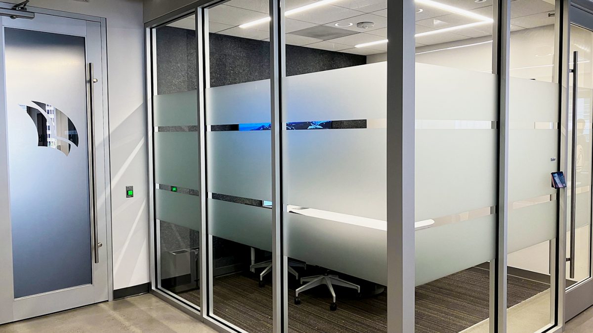 Photo of privacy film window graphics in Pitchbook office, produced and installed by SuperGraphics. Showcases glass windows to corporate office covered in dusted-crystal privacy film. Window film features cutouts to create design and branded elements.