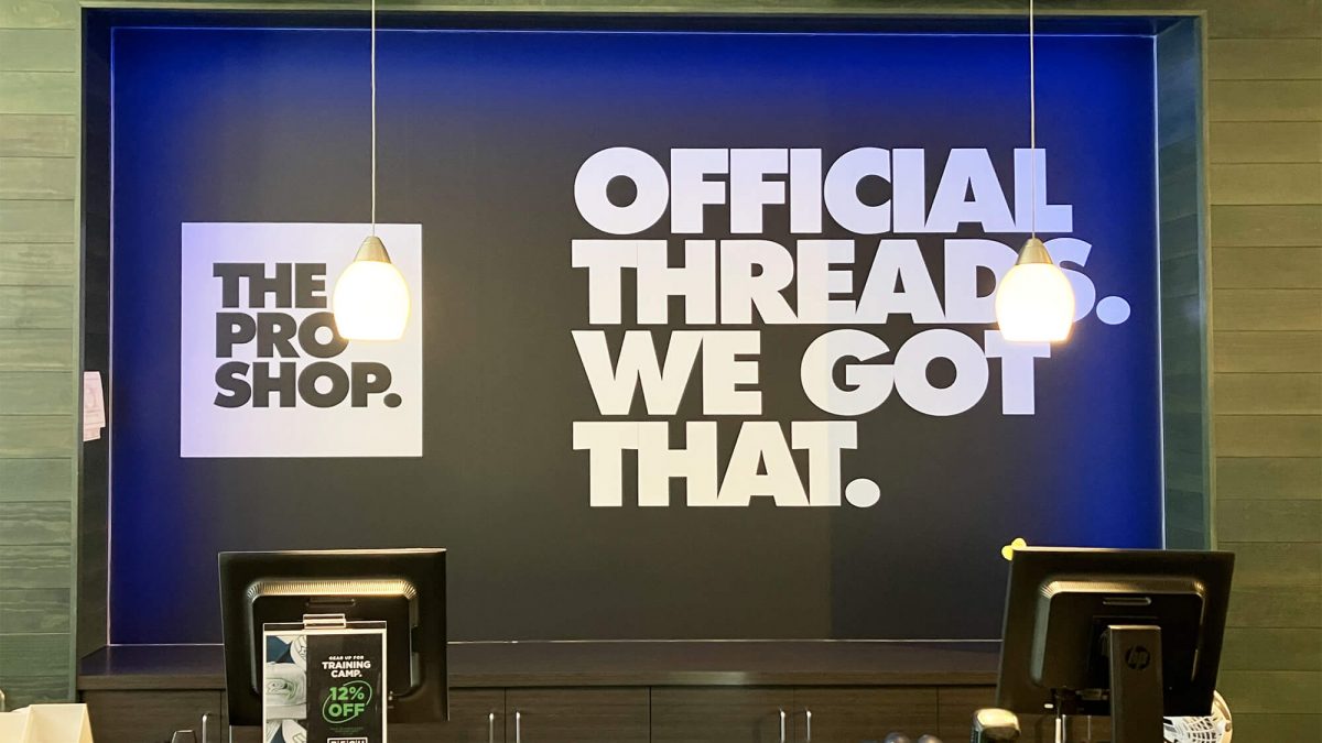 Pro Shop cash wrap, produced and installed by SuperGraphics. Showcases The Pro Shop logo and messaging, "Official Threads. We got that."