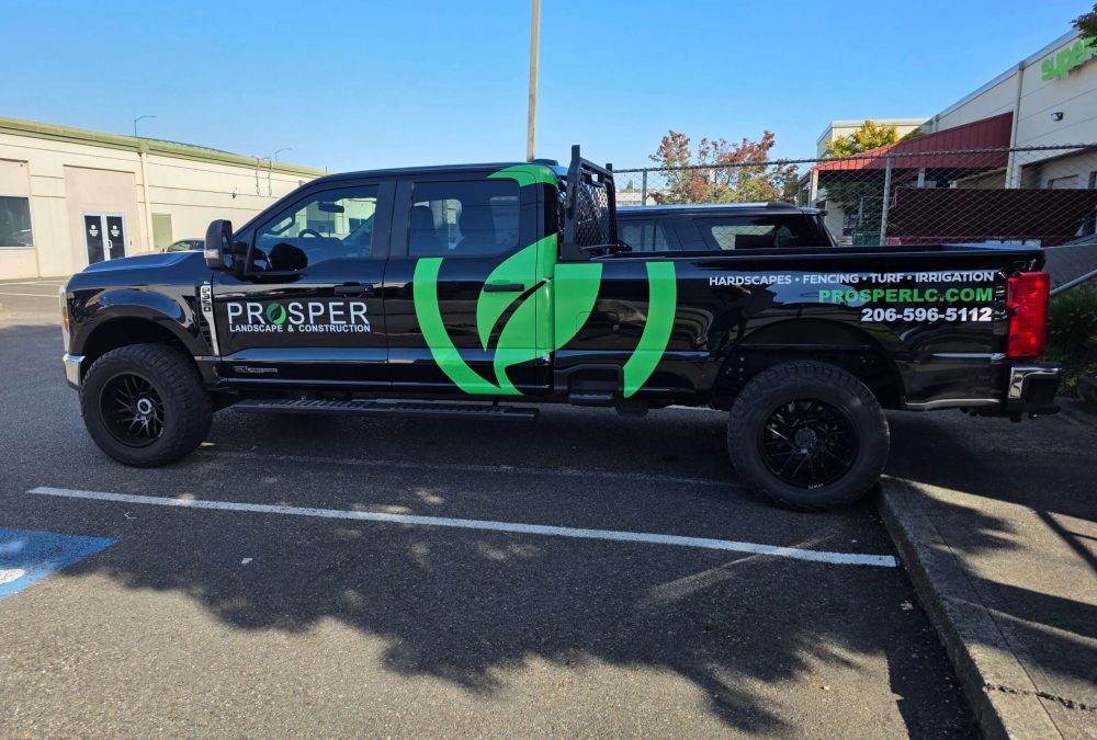 Black Prosper Landscape & Construction pickup truck with bold green graphic wrap and contact information, parked outside the SuperGraphics facility.