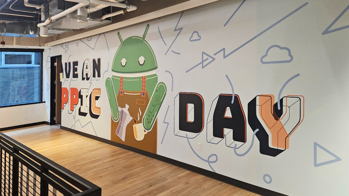 Photo of graphic mural installation completed on construction site, produced and installed by SuperGraphics. Wall mural graphic showcases "Have an Appic Day" with an Android icon pouring coffee.