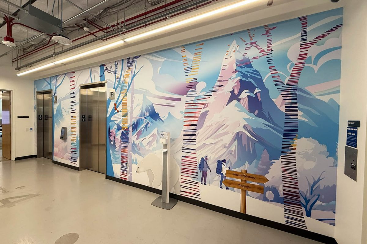 Colorful Snowflake office mural featuring a snowy mountain landscape, stylized trees with multicolored stripes, hikers, a polar bear, and a wooden sign pointing to Mount Whitney and Yosemite near the elevator bank.