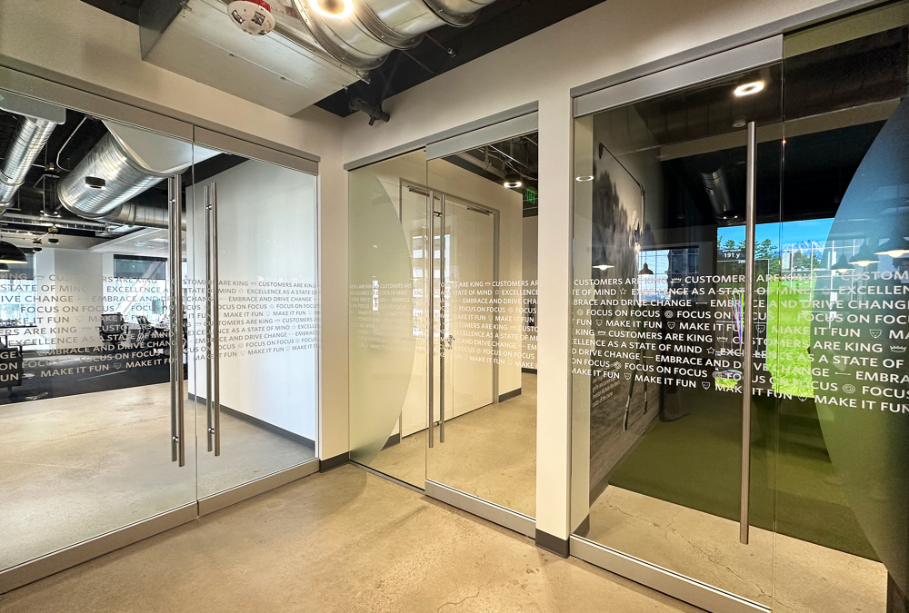 White printed privacy film on glass office doors with corporate mission statement text.