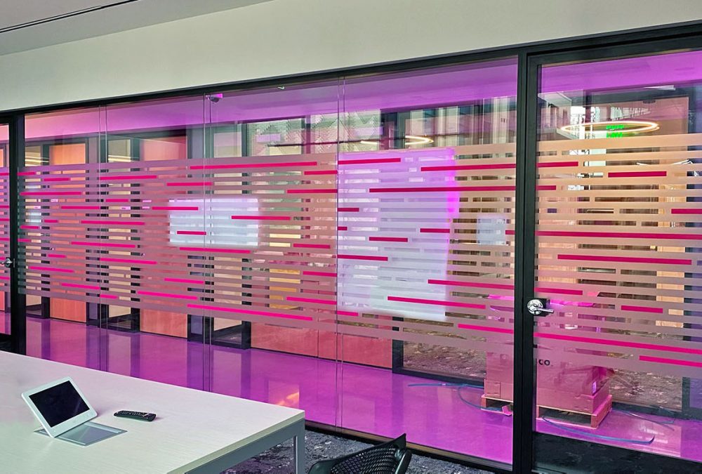 Privacy film in T-Mobile corporate office, produced and installed by SuperGraphics. Privacy film window graphics feature T-Mobile magenta, dusted crystal, and linear cutout design.