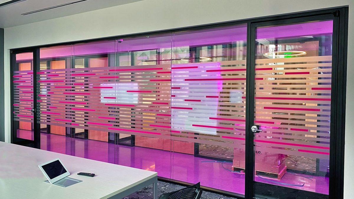 Privacy film in T-Mobile corporate office, produced and installed by SuperGraphics. Privacy film window graphics feature T-Mobile magenta, dusted crystal, and linear cutout design.