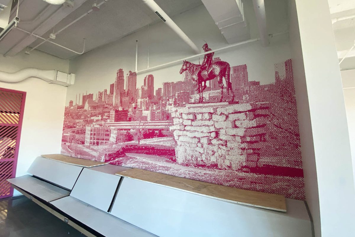 Large pink halftone mural featuring a city skyline and a statue of a rider on horseback, installed above built-in bench seating in an office space.