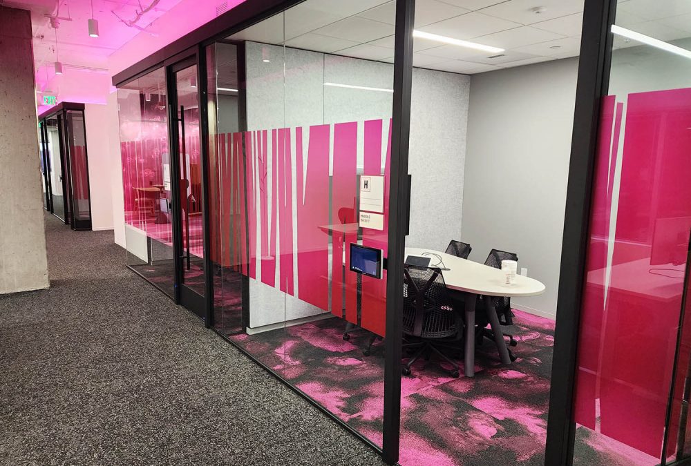 Glass-walled meeting rooms with magenta privacy graphics and pink accent lighting in a T-Mobile office.