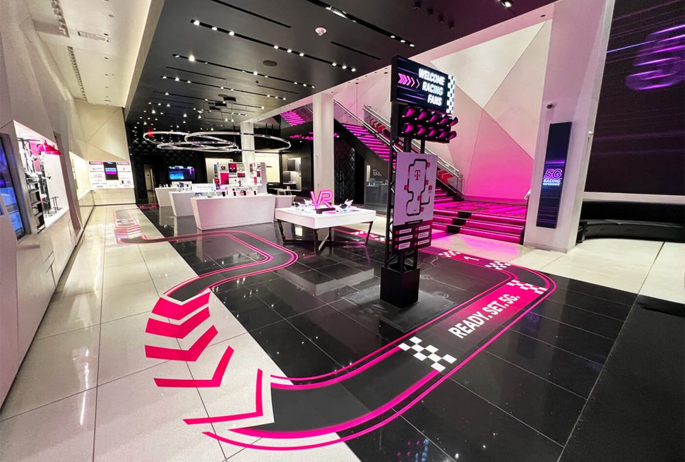 Store graphics for T-Mobile and F1 collaboration within T-Mobile flagship store. Shows pink racing floor graphics to guide customers through the store.