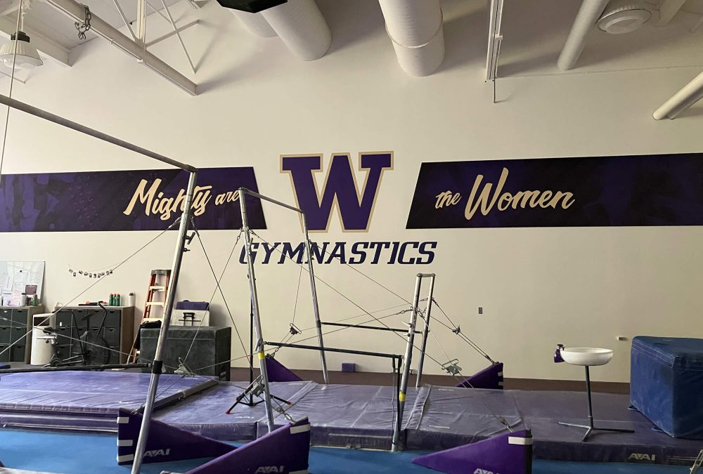 University of Washington Gymnastics wall mural, produced and installed by SuperGraphics. Showcases branded graphics and logos withe messaging, "Mighty the Women."