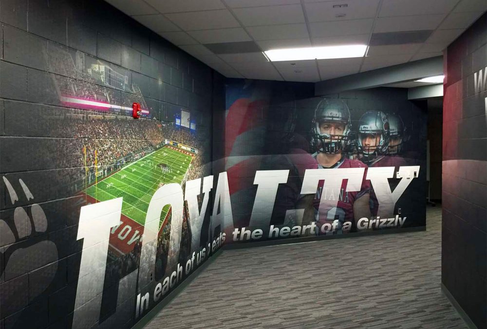 University of Montana wall graphic, completed by SuperGraphics. Showcases various football photography and brand messaging of 'loyalty' extending down hallway.