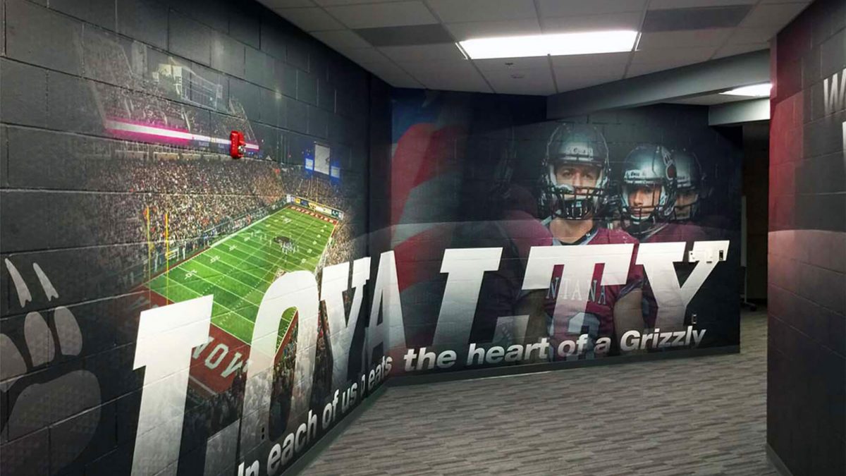 University of Montana wall graphic, completed by SuperGraphics. Showcases various football photography and brand messaging of 'loyalty' extending down hallway.