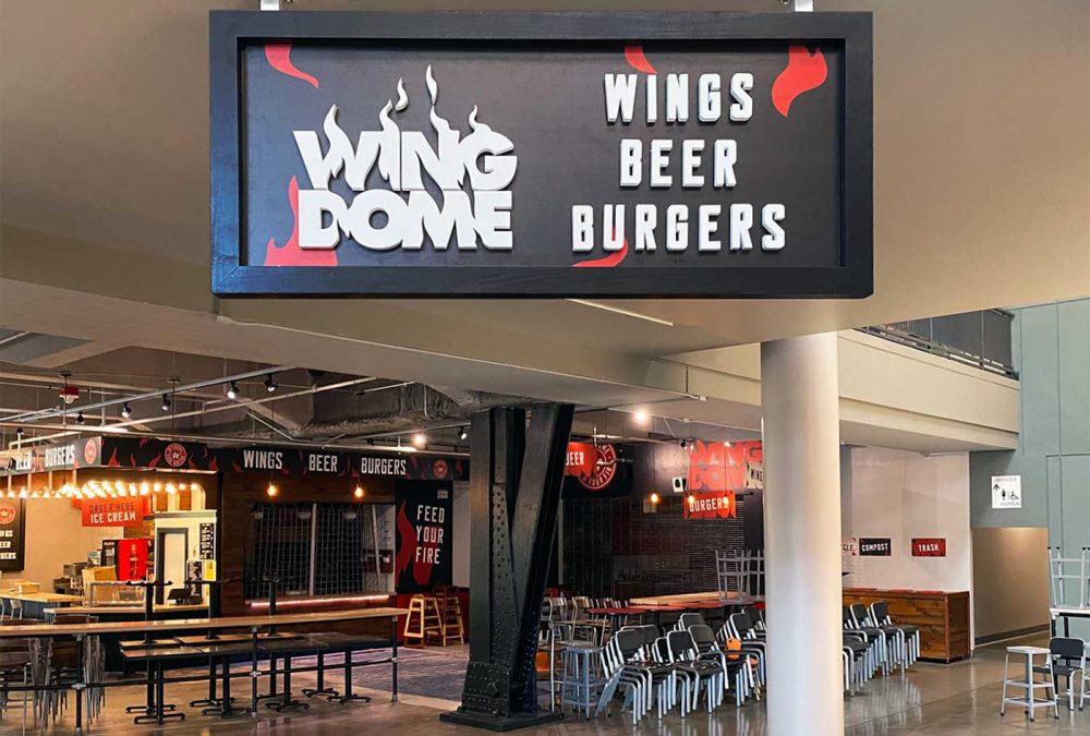 Wing Dome hanging signage, produced and installed by SuperGraphics. Features dimensional lettering and branded graphics on hanging sign.
