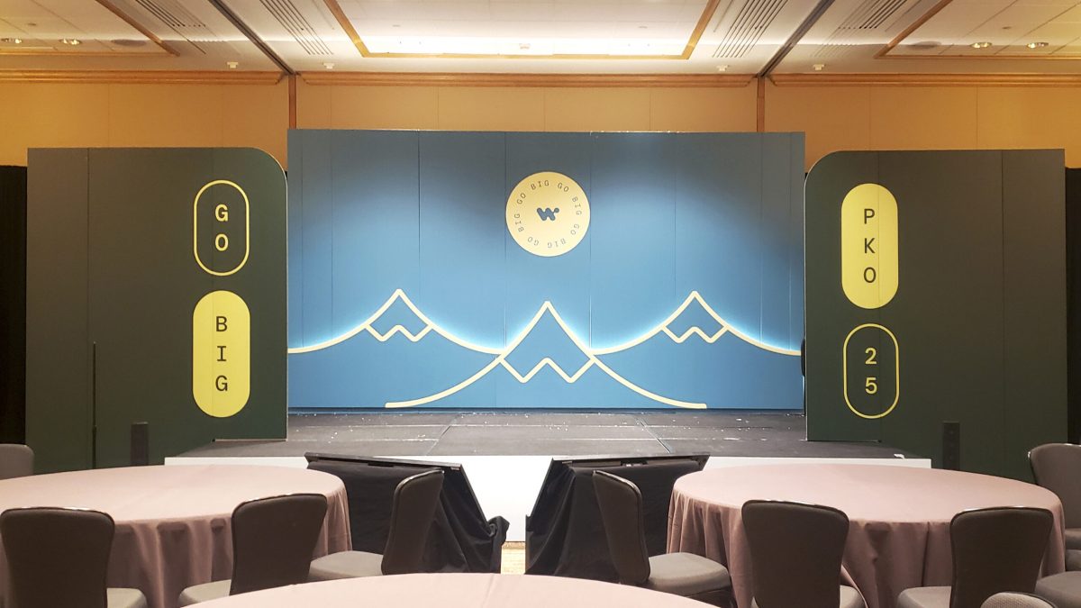 Trade show stage with large-scale EcoRigid printed backdrop featuring backlit mountain graphics and branding.