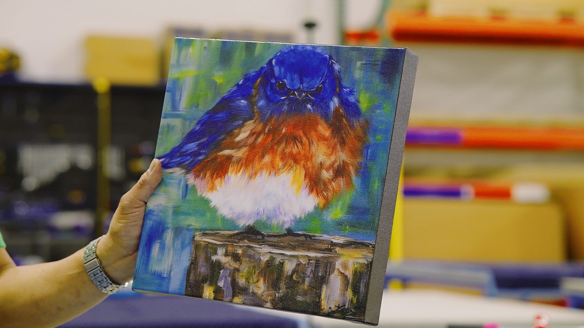 Photo of Fine Art Wrapped Canvas print produced by Northwest Fine Art Printing. Shows an employee holding up a Wrapped Canvas print of a painterly bird.