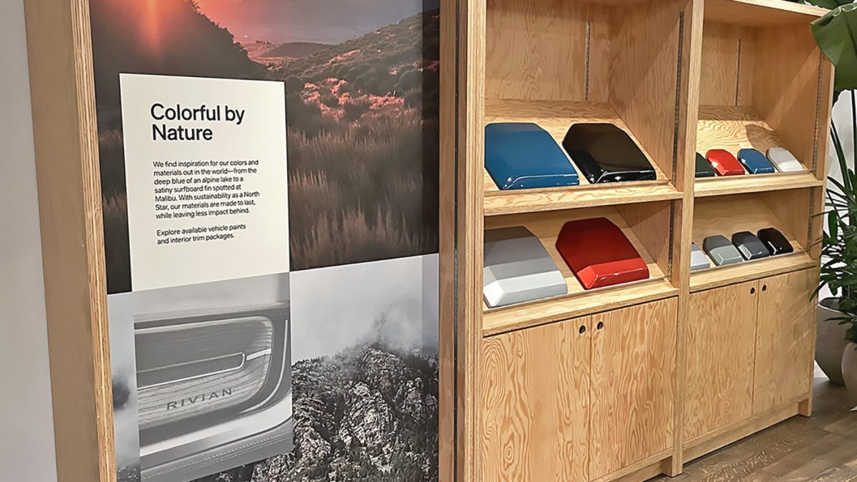 Inside the Rivian showroom, there is a wooden display showcasing various color options and materials for Rivian vehicles. The graphics above the display emphasize the natural inspiration behind the colors, blending aesthetic appeal with sustainability.